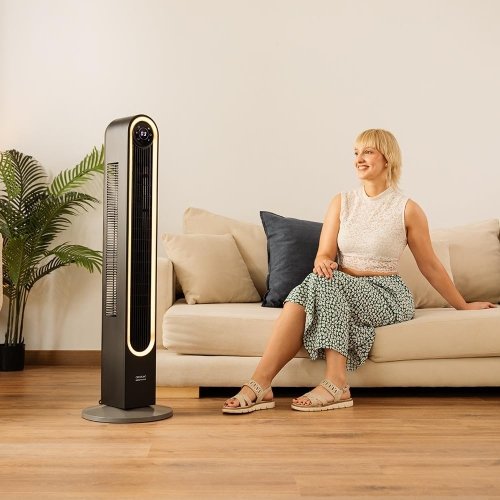 Mujer relajada junto a un ventilador inteligente Cecotec EnergySilence Skyline en un salón moderno 