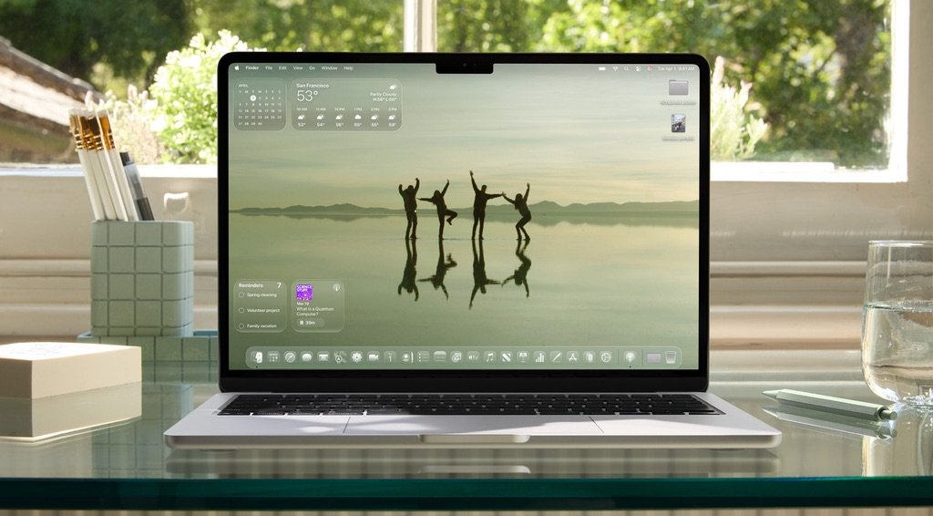 MacBook con macOS Tahoe mostrando la nueva interfaz Liquid Glass y widgets flotantes en el escritorio