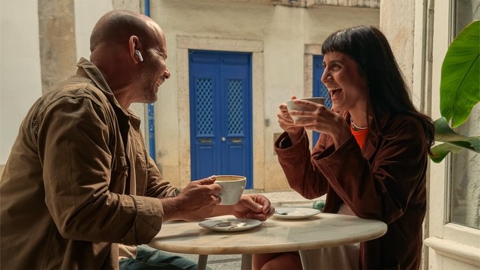 Pareja conversando en una cafetería con AirPods Pro 3, usando la función de Live Translation para comunicarse en distintos idiomas